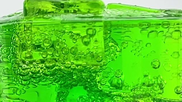 Close up pouring soft Drinks, green soda bubbles with ice into Glass Isolated