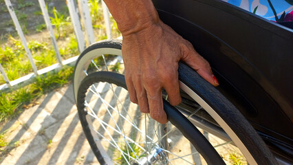 Selective focus hand of a wrinkled old woman with disability in a wheelchair tire