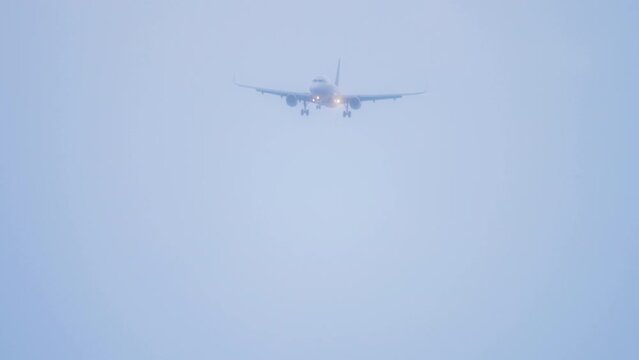 Jet airplane with lights on, approaching for landing, descent, arrival. Summer airliner in blue haze, fog, smog