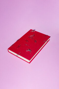 Red classic book and punch of silver paper clips lying on its cover 