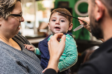 Young child looks curious while getting their haircut with a parent at a salon