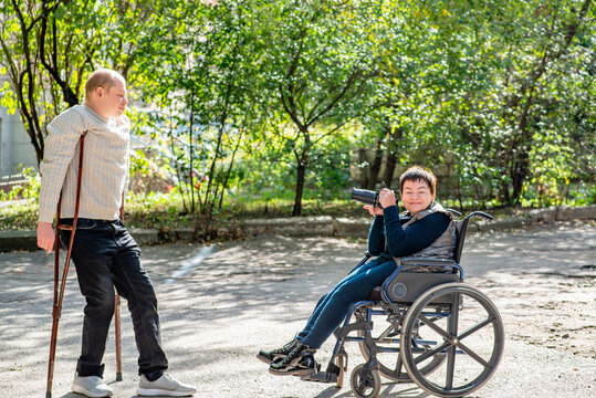 Young  woman in a wheelchair takes a picture of her friend