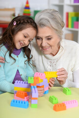 Cute girl and grandmother playing with colorful plastic blocks