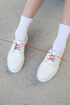 White shoes with one red lace/ribbon. Illustration of red thread 