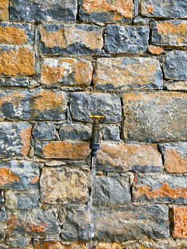 A stream of water from a metal faucet on rustic brick wall with crack