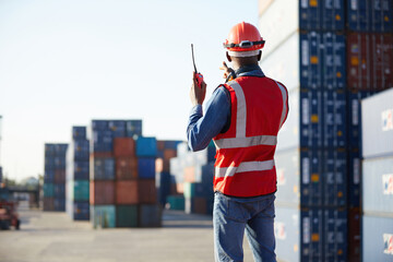 back view African factory worker or engineer using walkie talkie and showing stop gesture to crane car in containers warehouse storage