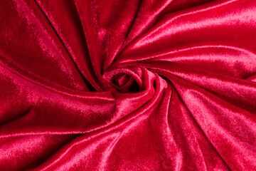 Textured background of deep red velvet fabric with folds.