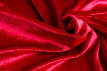 Textured background of deep red velvet fabric with folds.