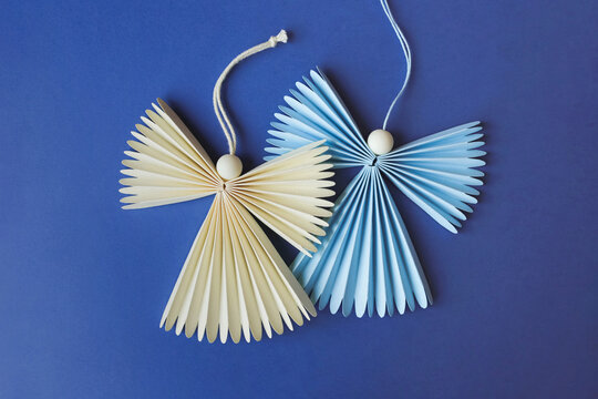 Two figures of festive angels made of paper laying on blue background