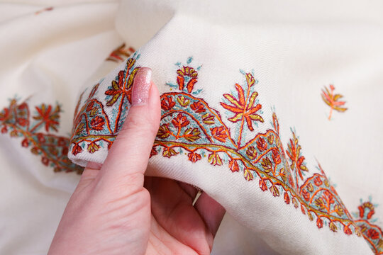 Hand with white traditional Kashmiri stitch embroidery scarf.