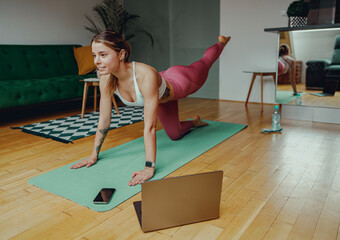 Young woman is practicing yoga on a mat in front of a laptop