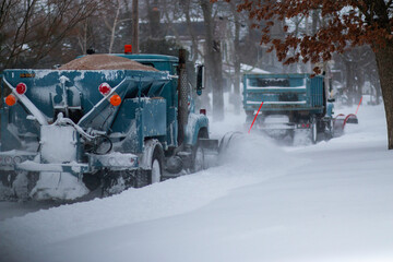 Two snowplows clearing a road and dropping sand