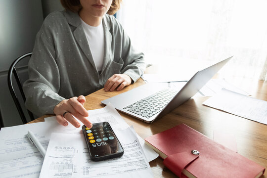 Crop woman using calculator in mobile phone while working with laptop