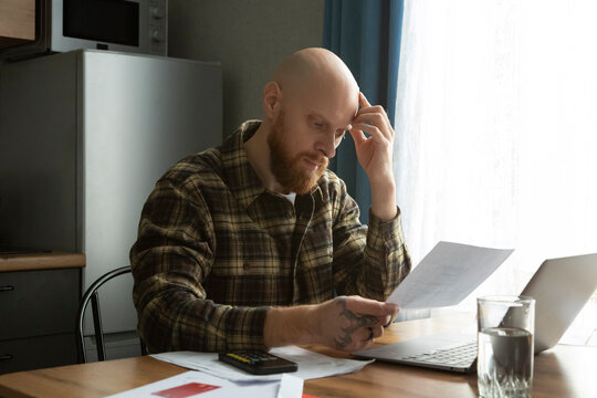 Focused man reading paper at table with laptop and water glass