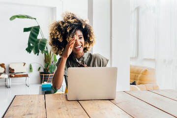Cheerful afro woman using laptop at home