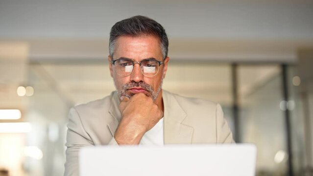 Busy mature business man trader broker analyst investor analyzing stock exchange trade crypto financial market looking at computer screen in glasses with charts reflection thinking of investing money.
