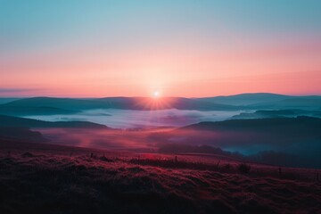Obraz premium Breathtaking sunrise over misty hills with a vivid gradient of pink and blue hues, casting a serene glow on the undulating landscape.