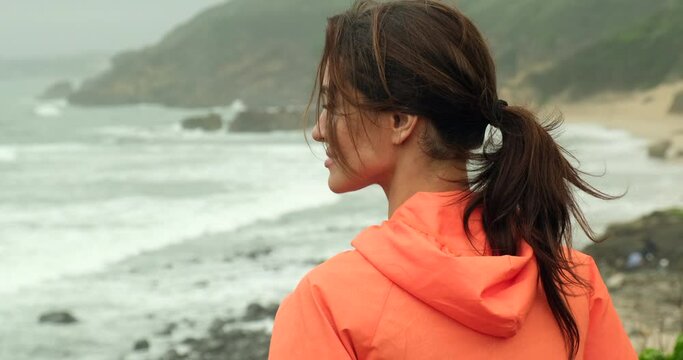 beautiful woman with cheekbones looks at the ocean and enjoys the view while relaxing. sporty girl after a morning jog breathes fresh sea air on the shore. athletic woman in a jacket 