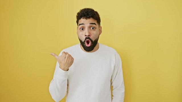 Cheerful young man, amazed by great discovery, pointing with an open-mouthed surprise to the side against a yellow isolated background