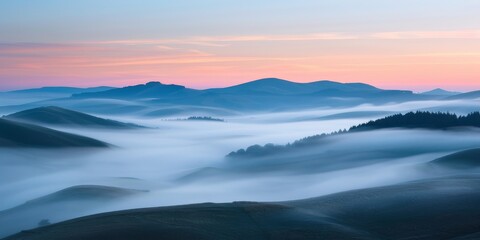 Obraz premium The sky is a beautiful shade of pink and orange. The mountains are covered in fog. The misty atmosphere gives the scene a serene and peaceful feeling