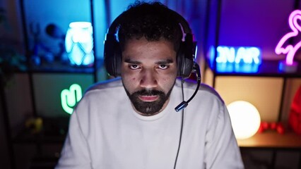 Focused man with headphones in a colorful gaming room at night.