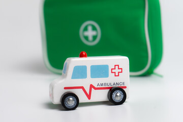 kids first aid kit, green bag with medical tools and wooden ambulance toy car isolated on white...