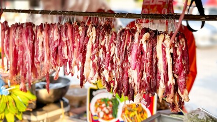 Dried meat hangs in an open-air market, a rustic Asian delicacy offered amidst a backdrop of fresh...