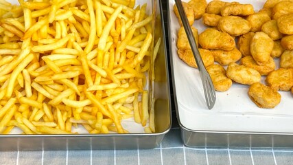 Crispy french fries and golden chicken nuggets are displayed in metal trays, ready for quick...