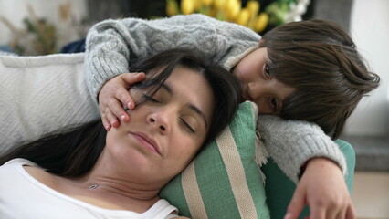 Son caresses mother while she rests laid on couch at home. Tender family relationship bond. Parent...