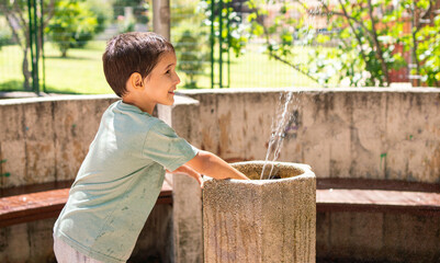 Close up of child playing at fountain in a public park at city.