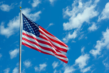 An American flag flutters in the wind against a blue sky with cumulus clouds. Generative AI