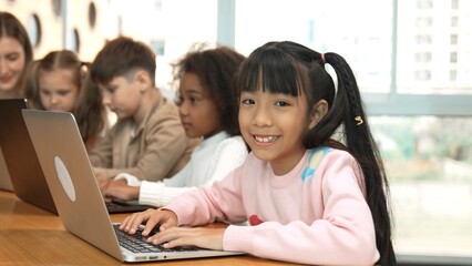 Asian girl working on laptop and looking at camera. Diverse children coding or programing...
