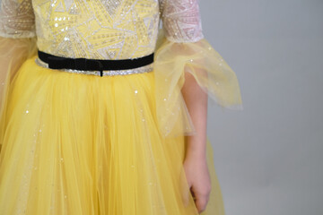 Close-up on ornate beadwork and sheer sleeves of a child's yellow gown, highlighting the elegance...