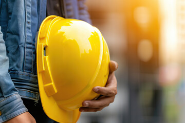 Yellow safety helmet in worker hands on blurred background