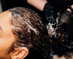 A young woman washes her hair with shampoo in a Barber shop. Professional hair care products.