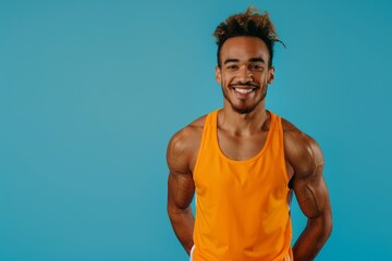 A smiling young man with an athletic build poses in an orange tank top for a portrait on a blue background - obrazy, fototapety, plakaty