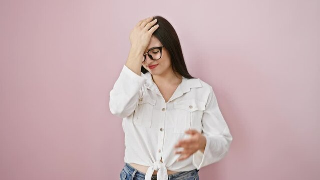 Oops! young, beautiful hispanic woman standing over isolated pink background, hand to head in regret. realized blunder too late, forgot crucial detail. stressed, confused by memory error.