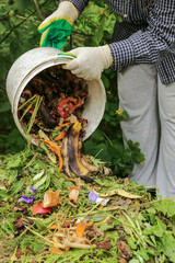 Compost heap pile with bio waste. Farmer hands put weeds grass plants, vegetable fruit scraps from...