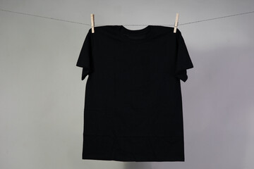 Black blank t-shirt hanging on clothesline with cloths pins gray background