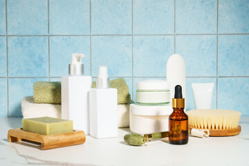 Natural cosmetic products in the bathroom, blue background. Soap, mask, face cream, serum bottle, jade roller.