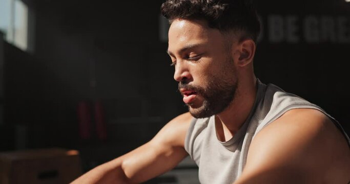 Break, fitness and sweat with sports man in gym to rest for recovery from training or workout fatigue. Breathing, exercise and health with tired young athlete sitting to relax in performance center