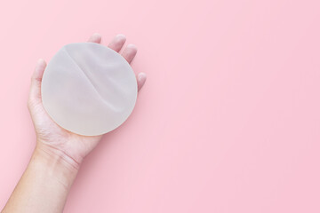 Top view silicone implants breast augmentation on space pink studio background, Gel type and rough touch surface in hand, Medical equipment used in clinic or hospital.