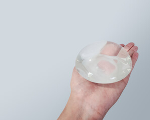 Silicone breast implant surgery gel type and smooth skin touch surface in hand on gray background, medical equipment.