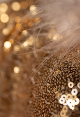 Vertical picture of gold glitter fabric with metallic shimmers and feathers. Bokeh background.Golden sequins in the form of rings. Close-up