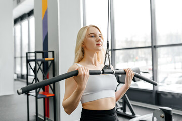 Fototapeta premium young athletic caucasian woman trains in fitness gym, doing thrust of upper block to chest, blond girl in white top and black leggings, healthy lifestyle concept