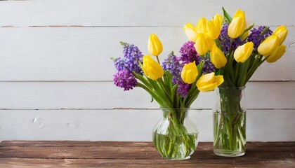 two vases filled with yellow and purple flowers on top of a wooden table in front of a white wall
