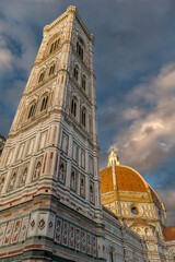 Florence, Italy - Giotto Campanile bell tower viewed with the dome of the Cathedral of Santa Maria del Fiore in Piazza del Duomo with warm sunset light on pictorial sky with clouds - obrazy, fototapety, plakaty