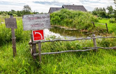 Abandoned fire pond overgrown with grass in a village. Text in russian: fire pond