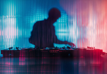 A DJ is mixing music on a turntable in front of a colorful, striped background.