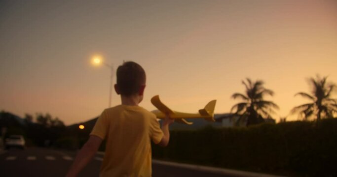 Happy kid runs with a toy airplane on park in the sunset light. Children play toy airplane. Little boy dreams of flying and becoming pilot. Child wants to become pilot and astronaut. Slow motion.